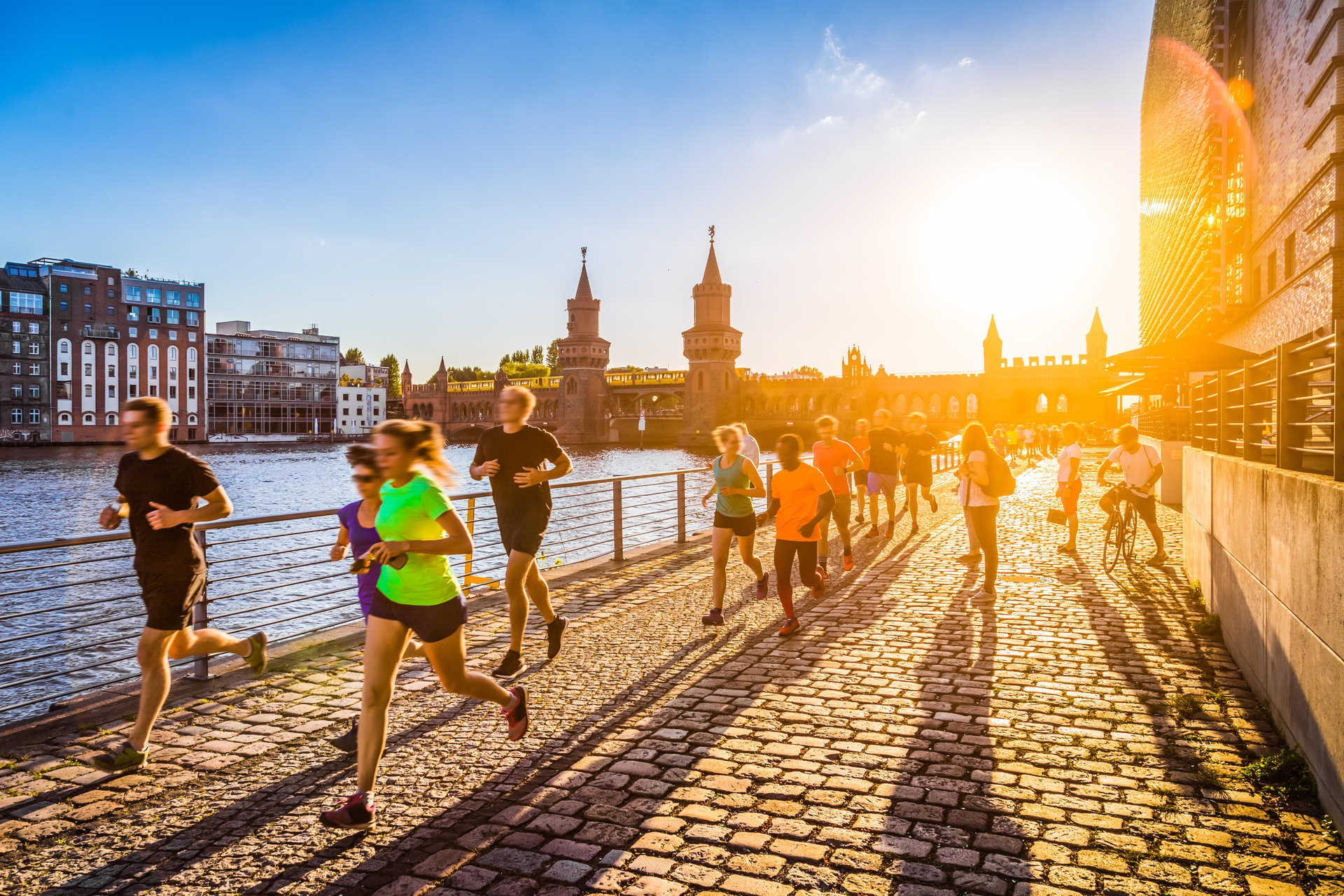 Runners by the Spree during the Berlin Marathon at sunset, featuring the Oberbaumbrücke in the background.