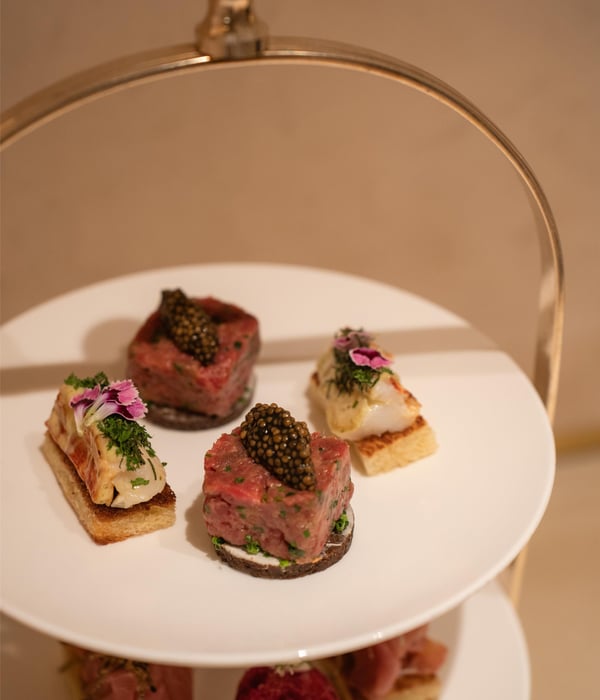 Three-tiered silver afternoon tea stand filled with gourmet savoury delicacies and canapés.