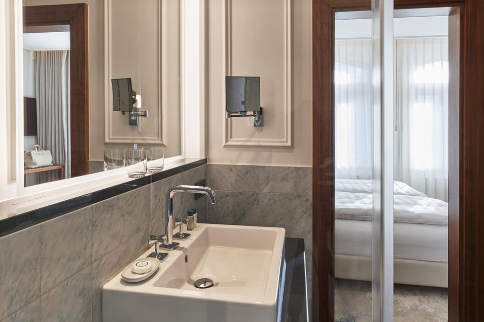Marble bathroom vanity with chrome fixtures and view into bedroom at Hotel Vier Jahreszeiten Kempinski München